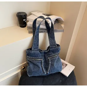 Detail of blue denim tote bag with washed texture and dual horizontal zipper pockets