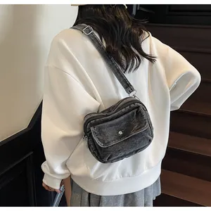 Detail of a dark grey washed denim crossbody bag with adjustable strap and metal button