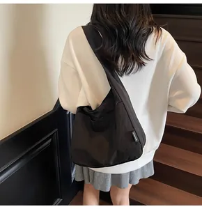 Detail of black slouchy nylon tote bag featuring wide shoulder strap and brand label