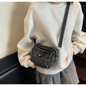 Detail of grey vintage denim crossbody bag with silver button on a casual outfit