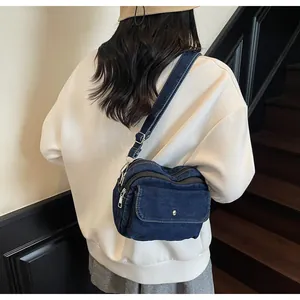 Detail of blue denim crossbody bag with multiple zippers and adjustable strap on stairs