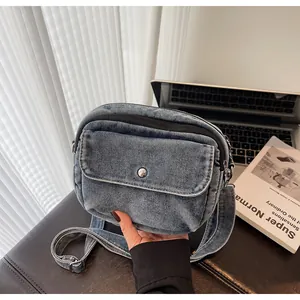 Close-up of retro blue denim crossbody bag featuring a front pocket and silver metal button