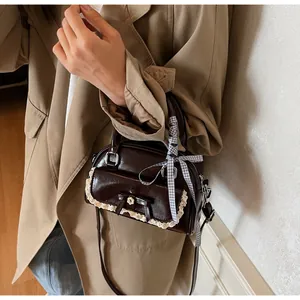 Détail du sac à main en cuir marron avec dentelle, nœud et ruban à carreaux sur l'anse