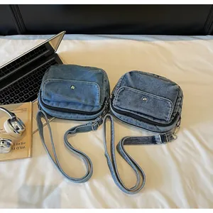 Detail of blue denim crossbody bag with adjustable strap and front metal snap pocket