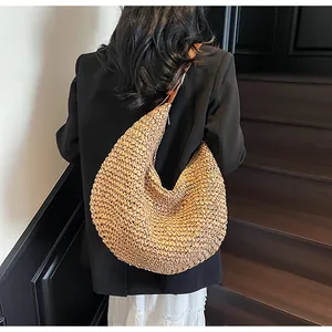 Detail of woven straw hobo bag with leather strap shown in a high-fashion lifestyle setting
