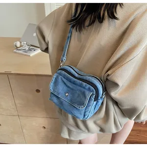 Detail of blue denim crossbody bag featuring double zippers and a front flap pocket