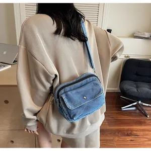 Detail of blue denim crossbody bag with metal snap pocket and zipper closure shown on a model