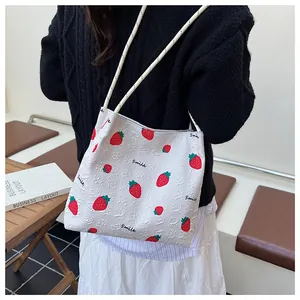 Detail of white strawberry print tote bag with Smile script worn by a model in a cozy setting