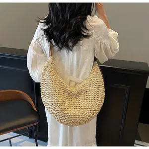 Close-up of a large crescent woven straw hobo bag featuring natural texture and brown strap