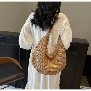 Detail of a large straw woven hobo bag with brown leather strap on a model