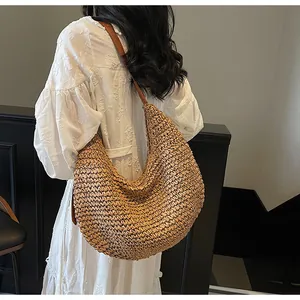 Close-up of a large woven straw crescent bag featuring a brown leather shoulder strap