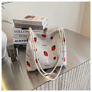 Detail of strawberry print tote bag showing embossed square texture and thin shoulder straps