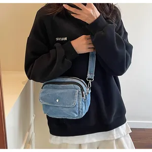 Detail shot of blue denim crossbody bag featuring double zippers and snap pocket