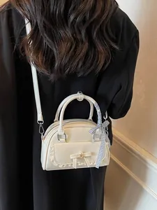 Sac à main vintage crème avec dentelle et nœud porté en bandoulière sur une veste noire