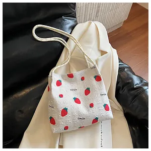 Close-up of strawberry print tote bag with grid texture and white rope shoulder strap