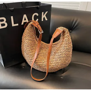 Close-up of woven straw crescent bag with adjustable brown leather shoulder strap