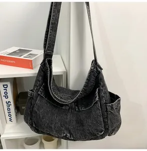 Detail of grey washed denim shoulder bag with large front pockets and wide strap