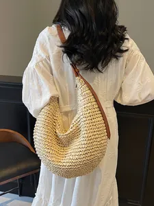 Large beige woven straw hobo bag with adjustable brown leather strap on model