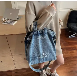 Detail der blau säuregewaschenen Jeans-Tote-Bag mit weißem Schriftzug und langen Trägern