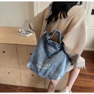 Detail der blauen Denim-Tragetasche mit Leisurely Carefree-Druck und verstellbarem Gurt