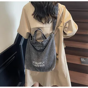 Detail der dunkelgrauen gewaschenen Denim-Tasche mit weißem Text und verstellbarem Gurt