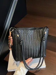 Handgewebte schwarze Eimertasche mit Holzperlenanhänger auf einem Vintage-Buch