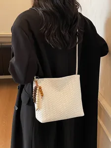 Weiße geflochtene Beuteltasche mit Holzperlenquaste auf einem schwarzen Blazer getragen