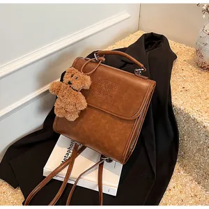 Detail of vintage brown leather backpack with embossed logo and plush bear charm