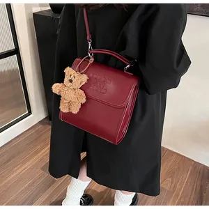 Macro shot of dark red textured leather bag with embossed letters and a teddy bear charm