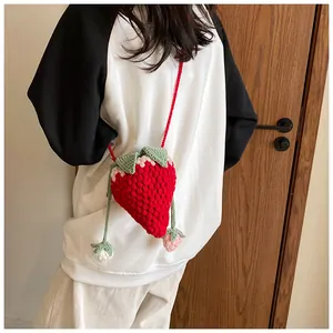 Detail of a handmade crochet strawberry crossbody bag with green leaves and red yarn texture