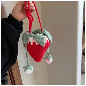Close-up of handmade crochet strawberry bag featuring red yarn textures and green leaf detail