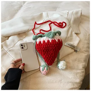 Detailed macro view of a handmade crochet strawberry bag with red yarn texture and leaf accents