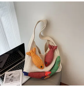 Detail of beige knit hobo bag featuring colorful fish plush charms and textured weave