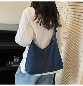 Detail of a large dark blue denim hobo bag worn by a model in a minimalist room