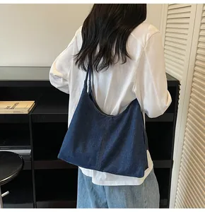 Deep blue denim tote bag with curved opening shown over the shoulder in a minimalist room