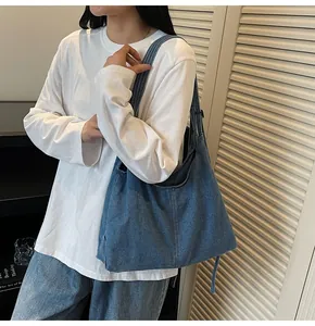 Detail of a large denim crossbody bag with wide shoulder strap worn by a model