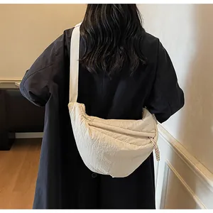 Rear view of a model wearing the cream-colored nylon dumpling bag with adjustable strap