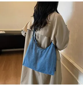 Detail shot of a large capacity blue denim hobo bag worn with a beige trench coat