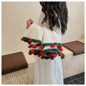 Close-up of hand-crocheted cream shawl with green scalloped edges and red cherry detail