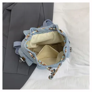 Top view of denim backpack showing beige lining, interior pocket and ethnic wood beads