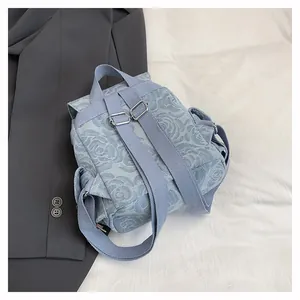 Detail of light blue denim mini backpack with rose pattern and silver metal buckle