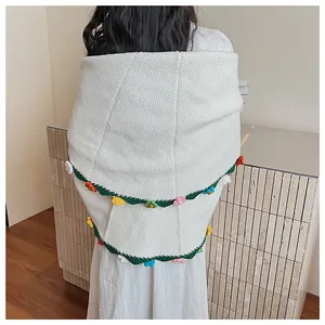 Detail of white knit shawl featuring green scalloped edges and colorful crochet flowers