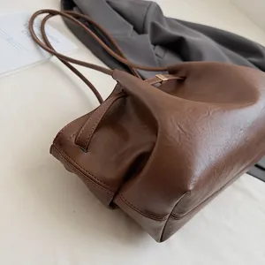 Détail du sac seau en cuir marron foncé montrant le grain riche et les garnitures dorées