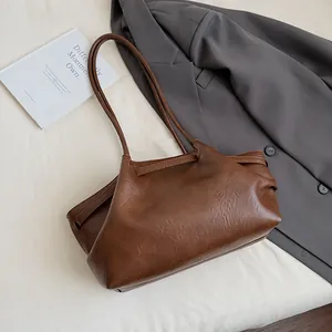 Détail d'un sac cabas marron vintage posé sur un blazer gris avec un livre