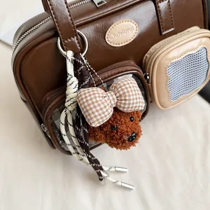 Detail einer dunkelbraunen Boston-Tasche aus PU-Leder mit Seitentaschen und Teddybär-Anhänger