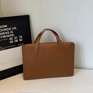 Detail of a brown leather laptop bag showing reinforced handles and smooth finish