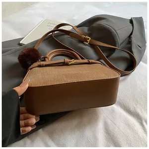 Detail view of brown leather bucket bag with textured weave and red plush charm accessory