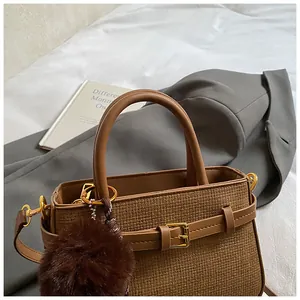 Detail of brown woven crossbody bag with golden hardware and fuzzy pompom accessory