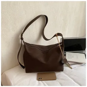 Brown canvas crossbody bucket bag with adjustable strap shown with daily laptop essentials