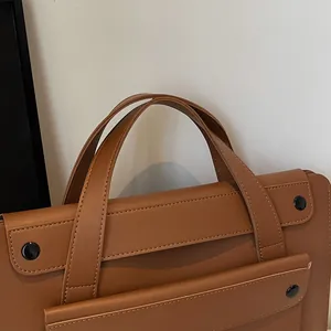 Detail view of a brown leather business briefcase showing dual handles and sleek stitching